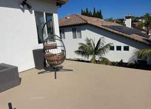 Rooftop patio with a hanging egg chair, tan flooring, white walls, and a view of neighboring houses and palm tree.