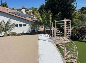 Rooftop terrace with white wall, wooden railing, curved stairway, and palm trees beside a house