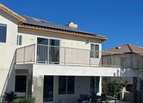 Two-story beige house with a balcony, white trim, and a tiled roof under a clear blue sky