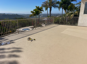 Sunlit patio with metal railing, palm trees, and a distant landscape view