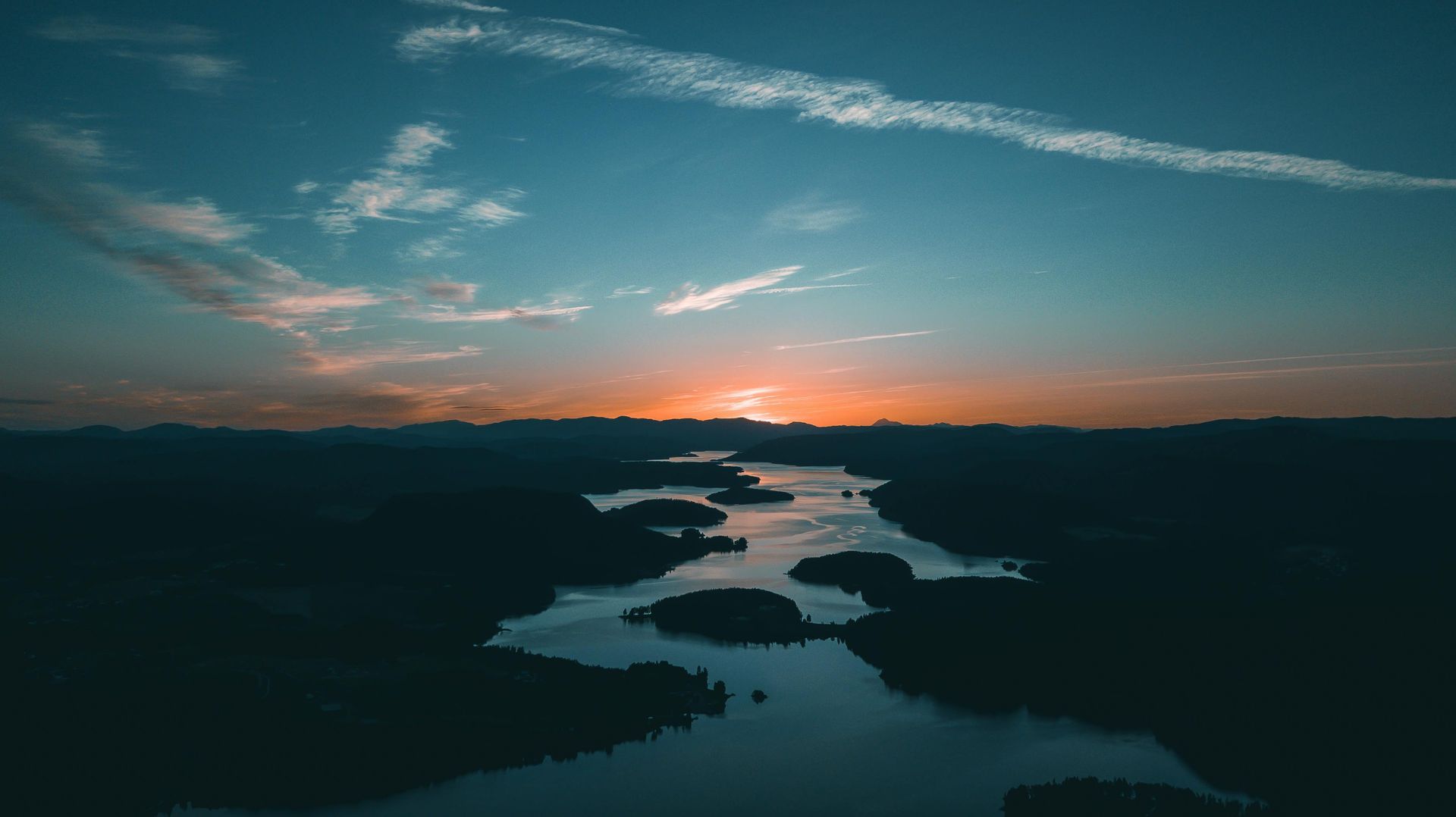 Sunset over winding river, dark silhouettes of land, blue and orange sky.