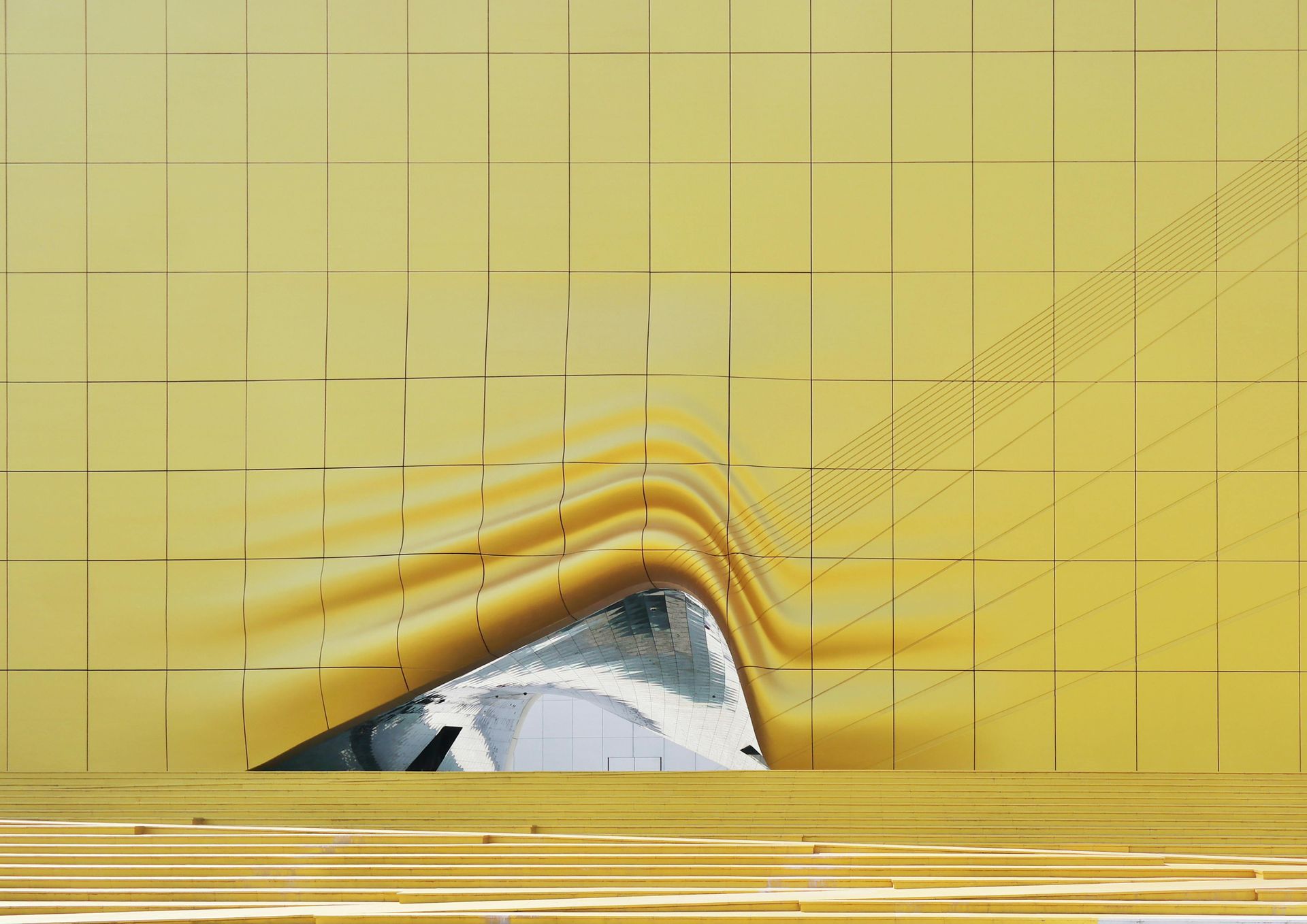 Gold-toned building facade with a triangular opening revealing a mirrored interior.