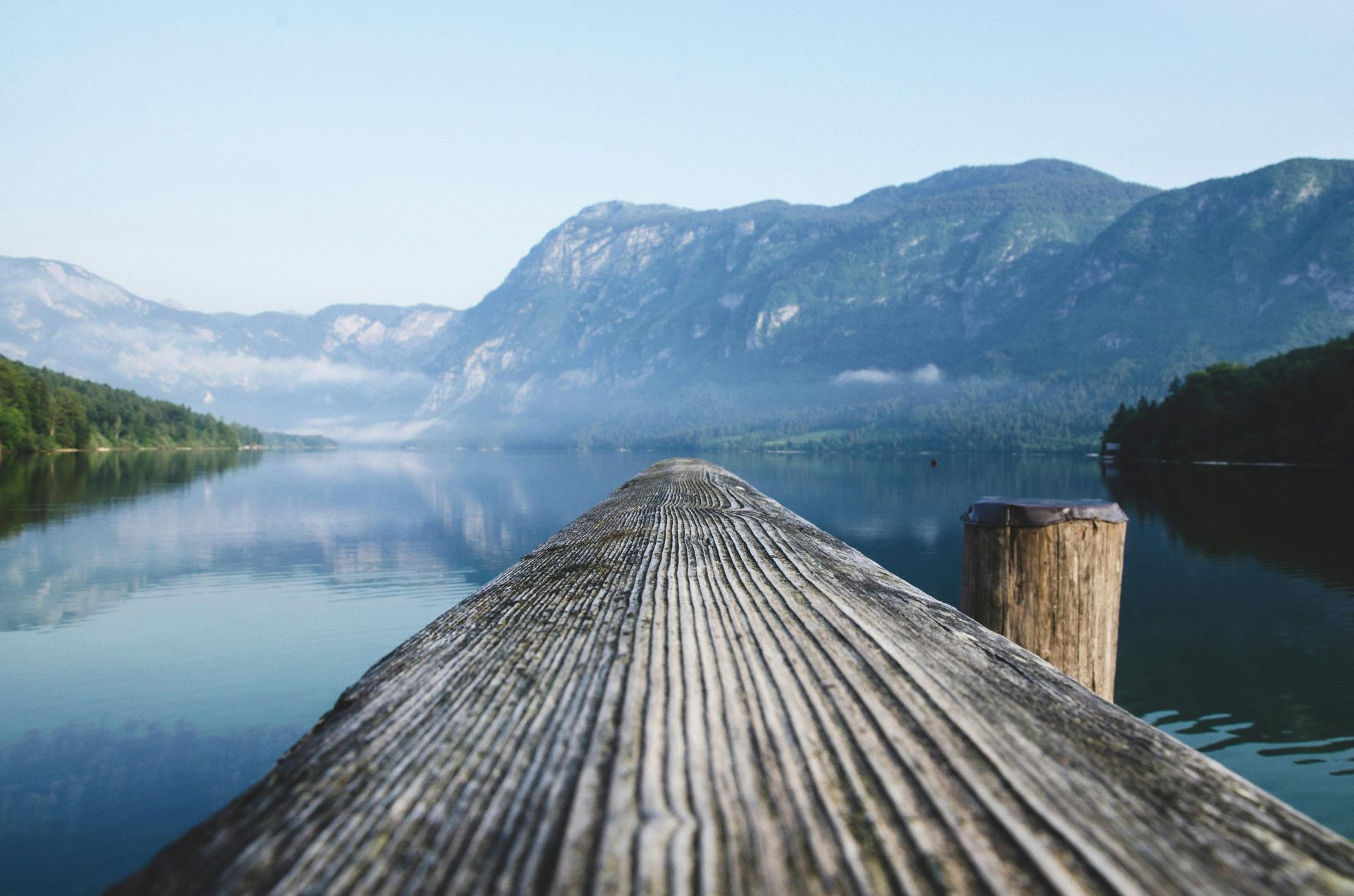Wooden dock extending into still lake, mountains in the background, misty sky.