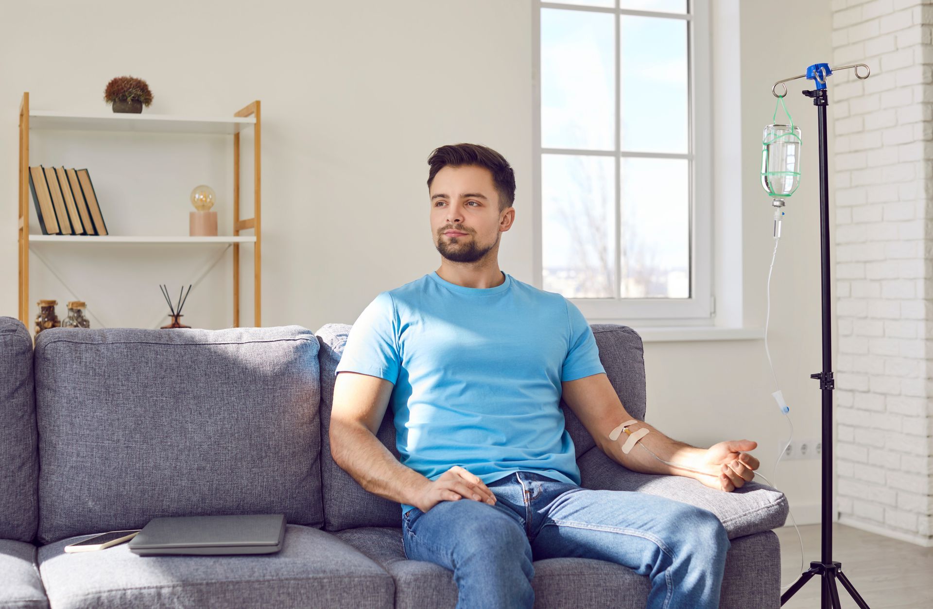Man sitting on a gray couch in a bright living room, with a TV camera on a tripod nearby.