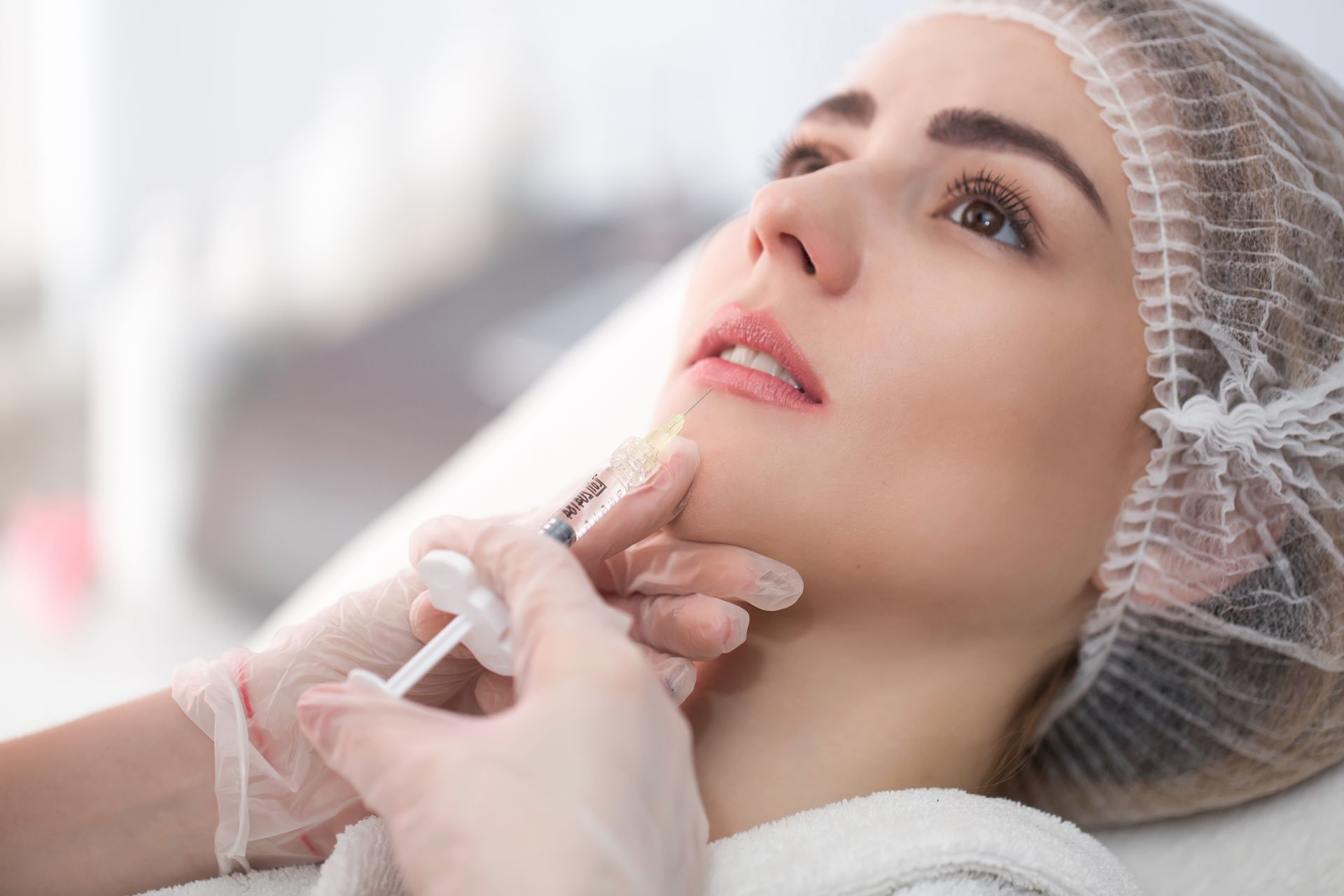 Woman receiving a facial injection while lying back with a protective cap on in a spa treatment setting