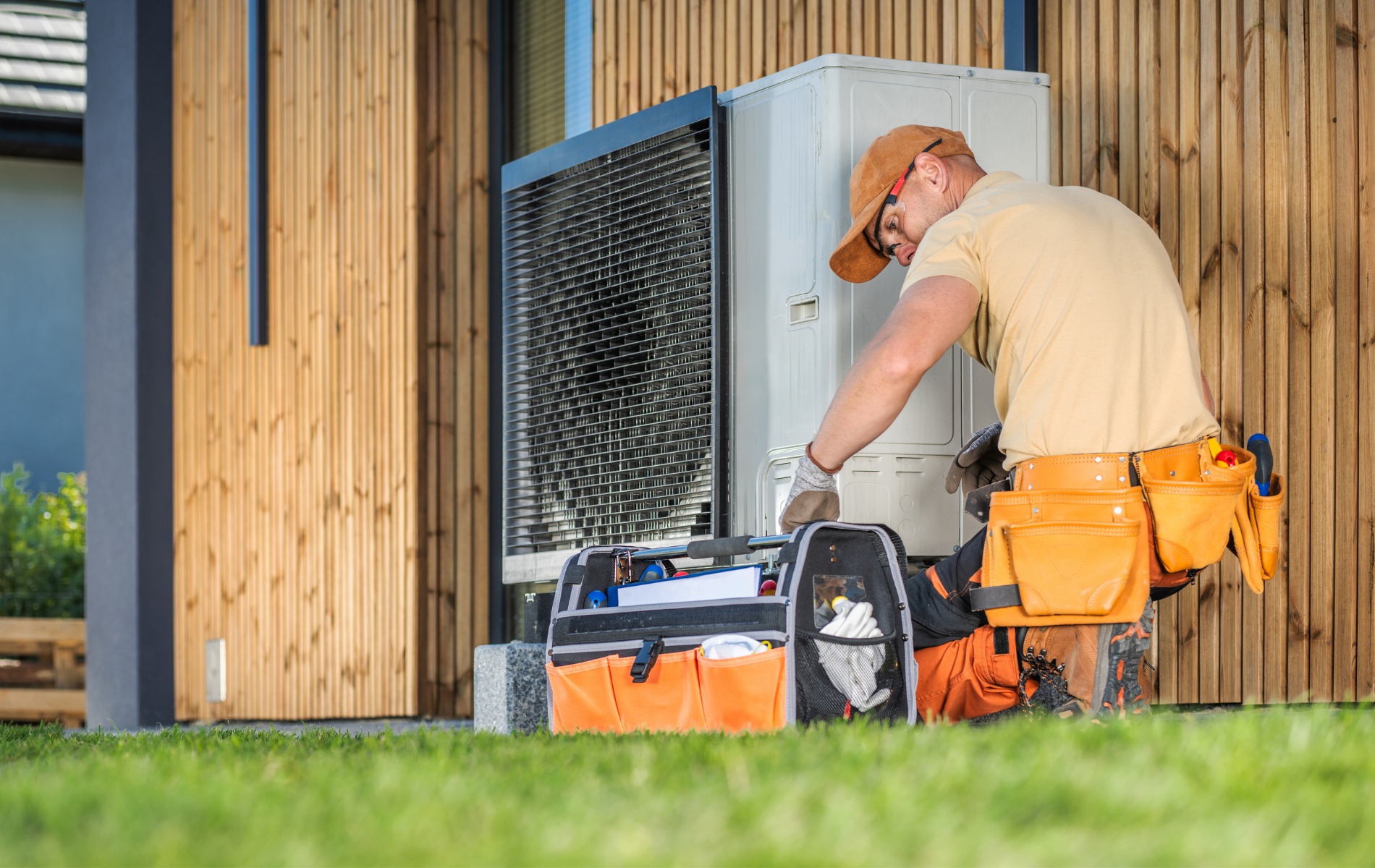 Technician in orange tool belt servicing outdoor HVAC unit. Tools are in an open toolbox.