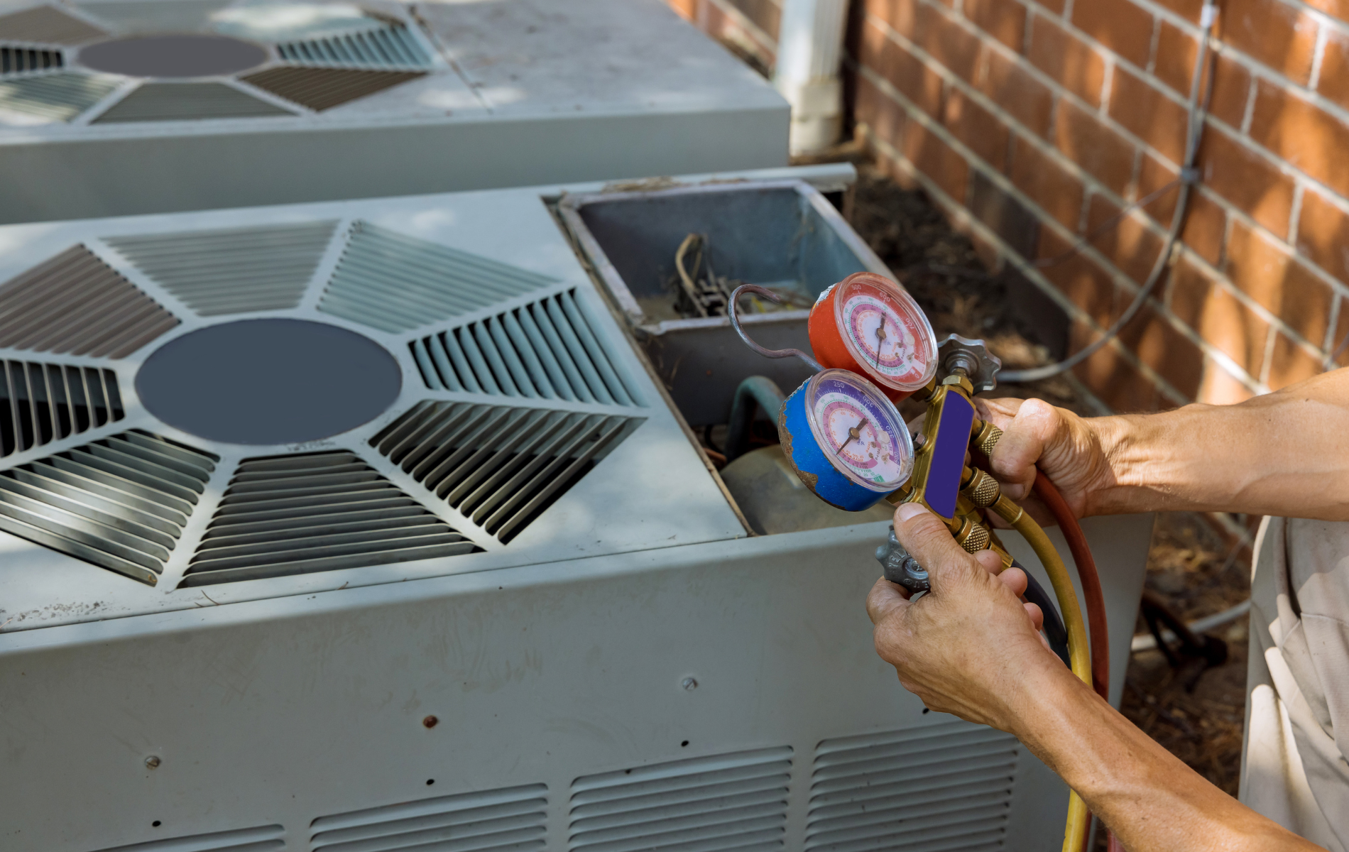 HVAC technician servicing an air conditioning unit; gauges and hoses connected.