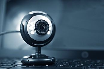 Webcam mounted on a laptop, black and silver, with lens and attached cable.