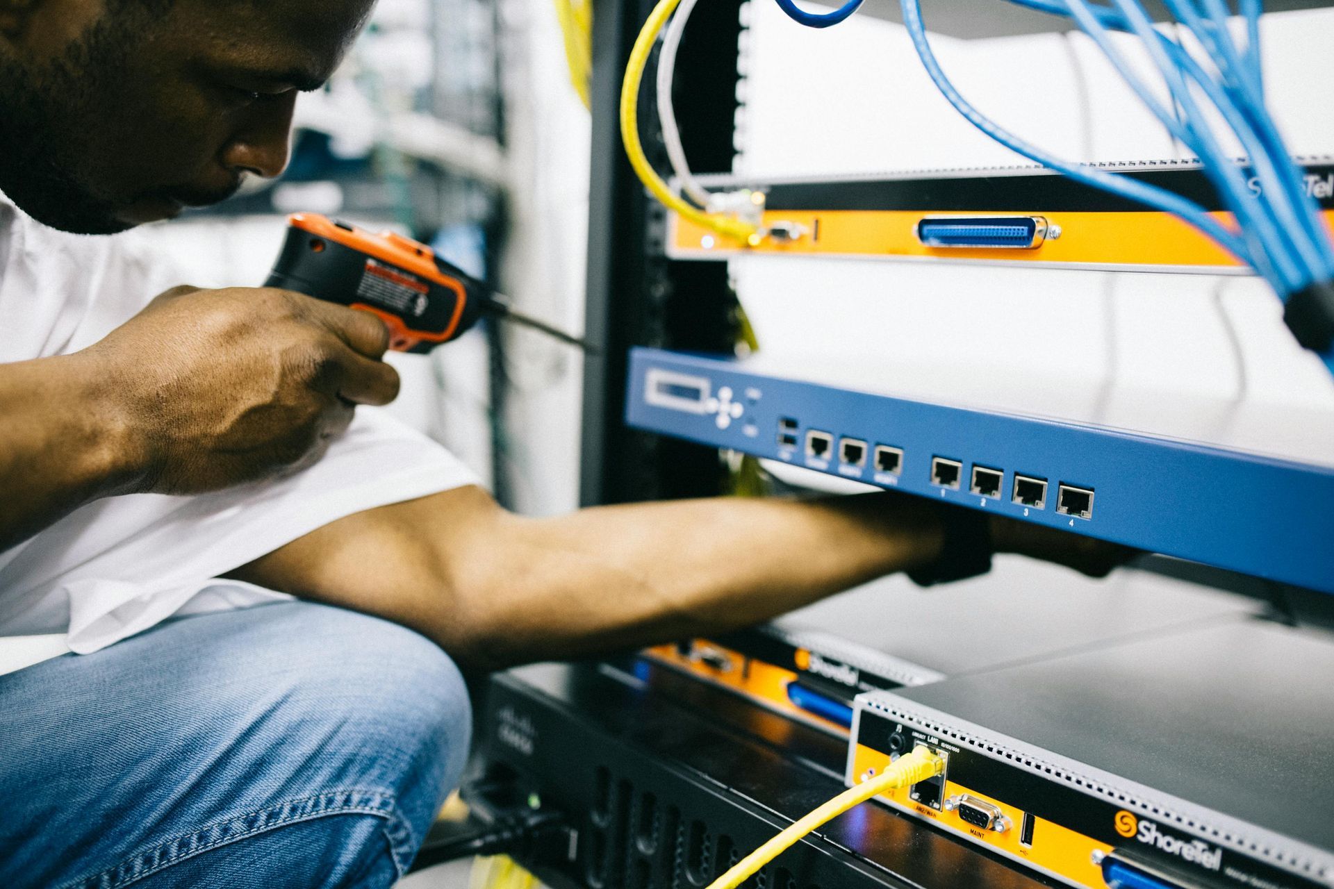 Technician using a handheld tester to inspect blue network equipment in a server rack