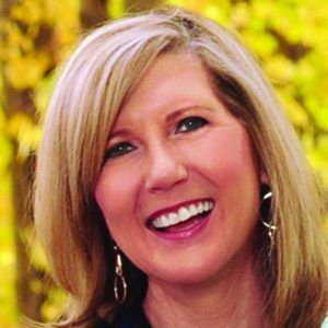 Smiling blonde woman with shoulder-length hair against a yellow floral background
