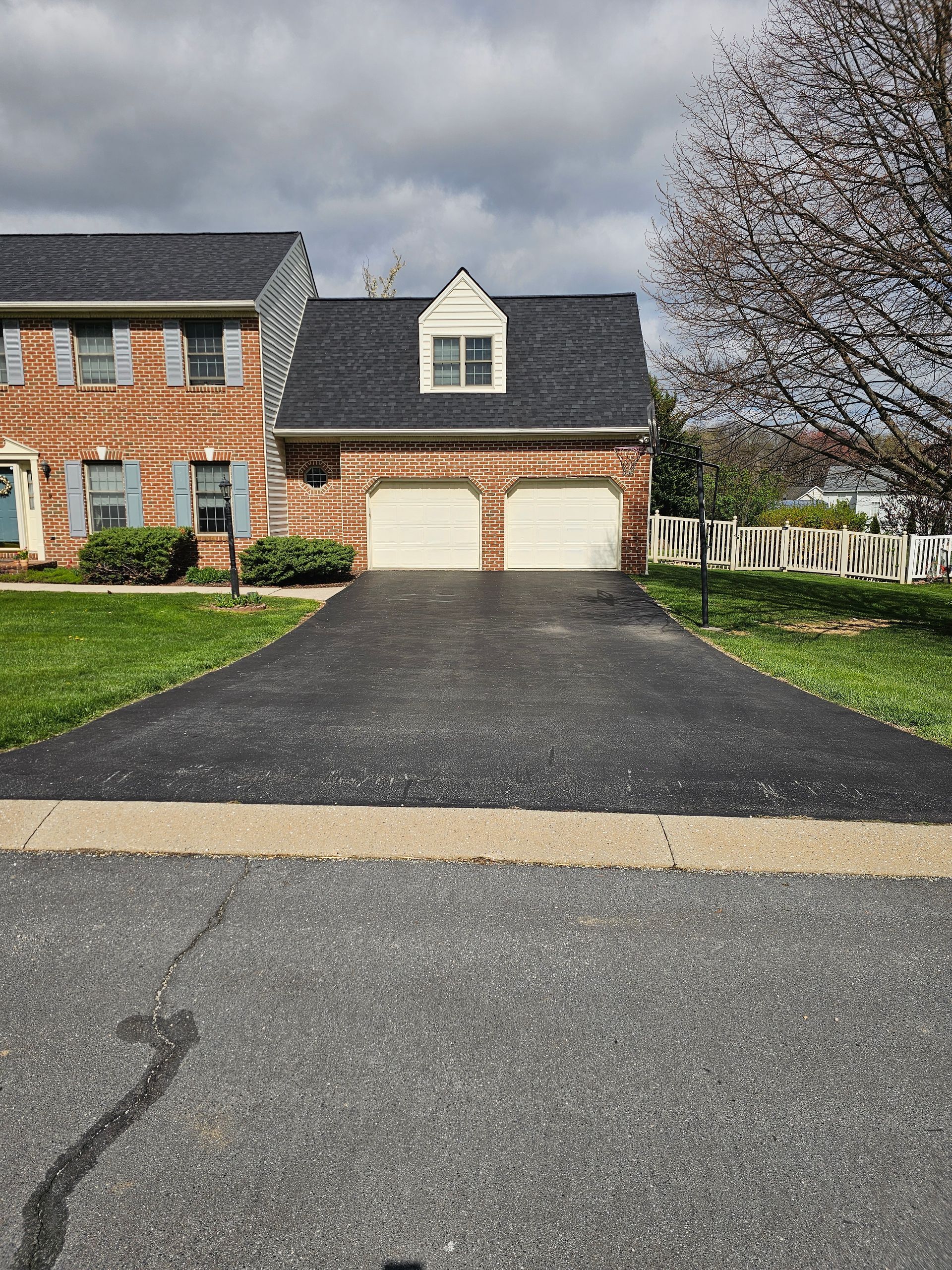 Suburban brick house with a two-car garage and black driveway under a cloudy sky