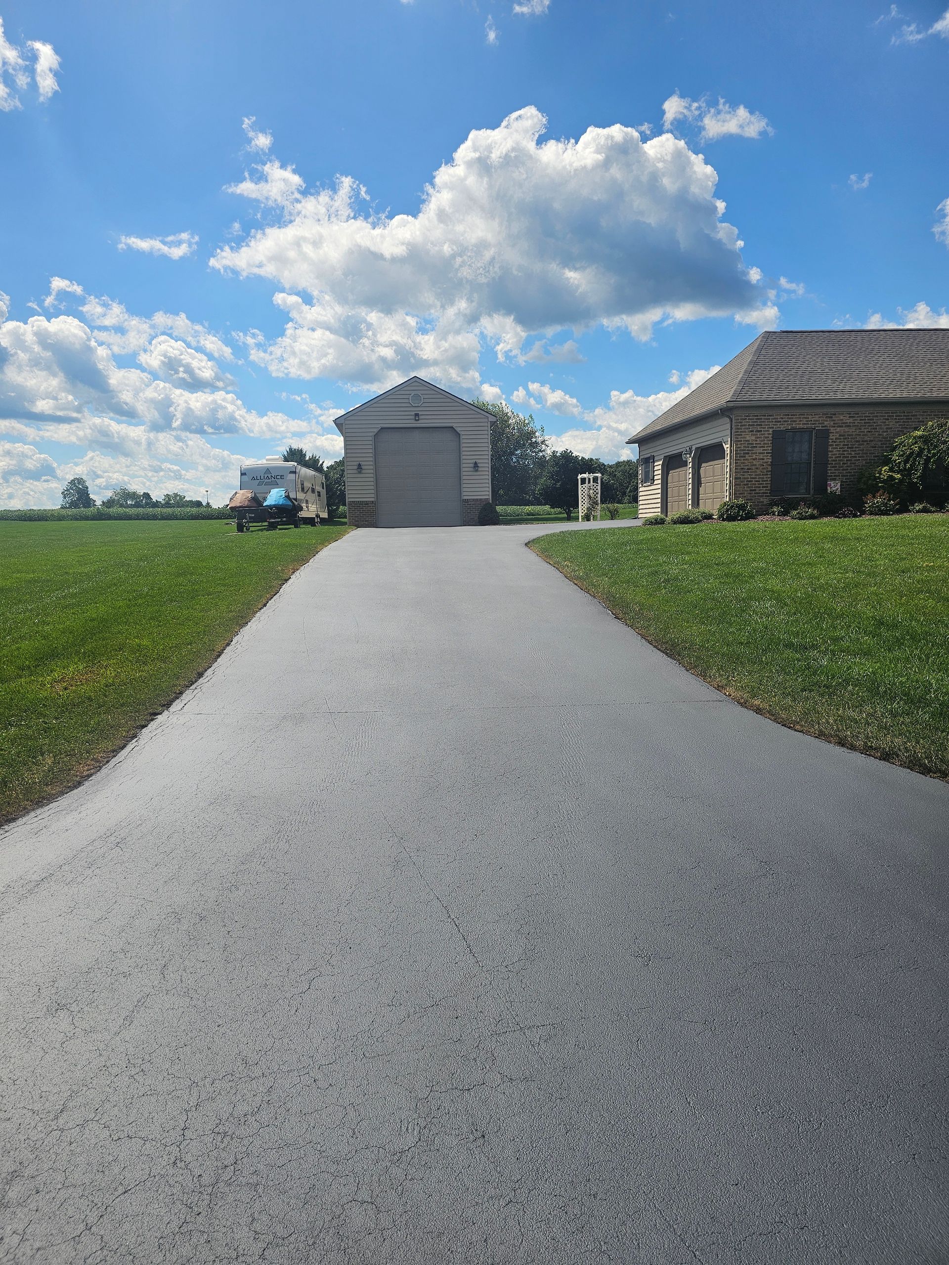Gravel driveway leading to a white garage and house under a blue sky with clouds.