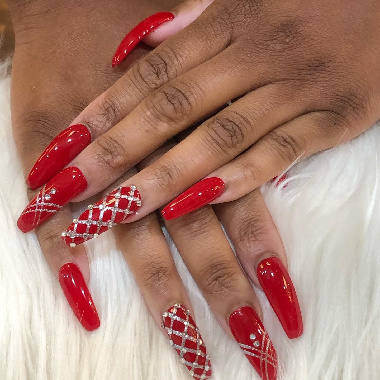 Hands with long, glossy red nails, some featuring intricate silver lattice designs and small rhinestones.
