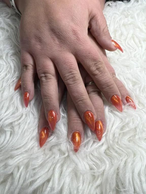 Close-up of hands resting on a white faux fur surface, showcasing vibrant, glossy, almond-shaped orange nails.
