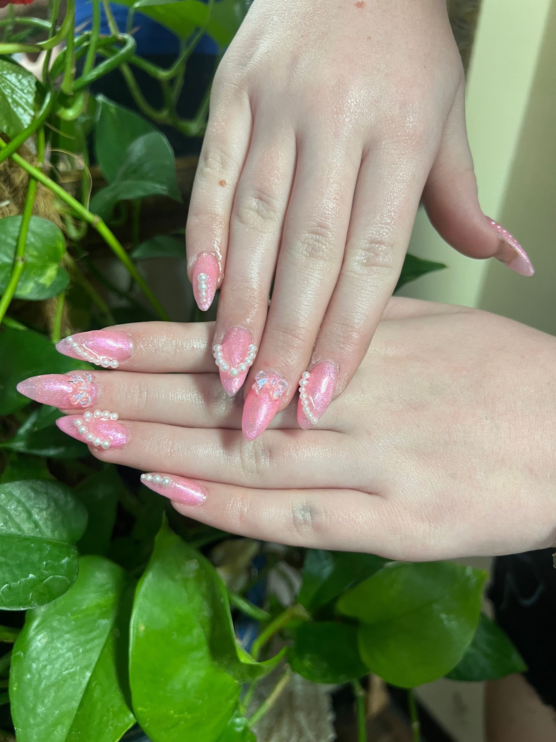 Two hands with pink almond-shaped nails, accented with white lace-like patterns, held over lush green foliage.
