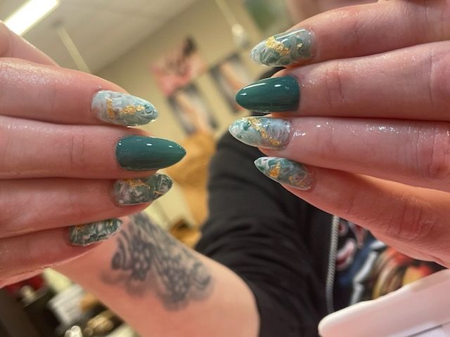Hands with almond-shaped nails in dark teal and marbled blue-and-white patterns with gold foil accents.
