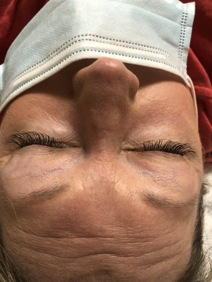 A close-up view of a person’s closed eyes, highlighting their long, dark eyelash extensions and a light blue face mask.