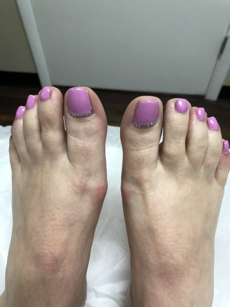 Close-up of two feet with light purple, manicured toenails and small decorative rhinestones at the base of each big toe.