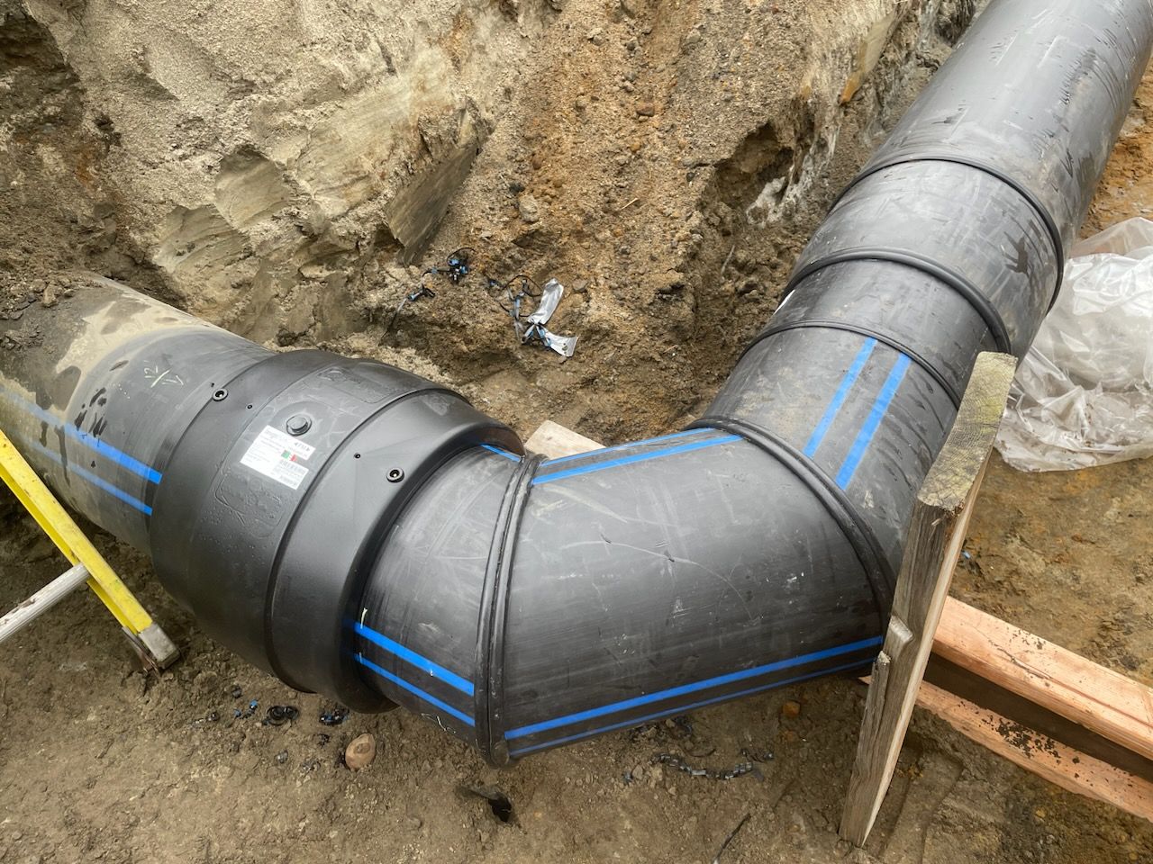 A large black pipe is being installed in the dirt.
