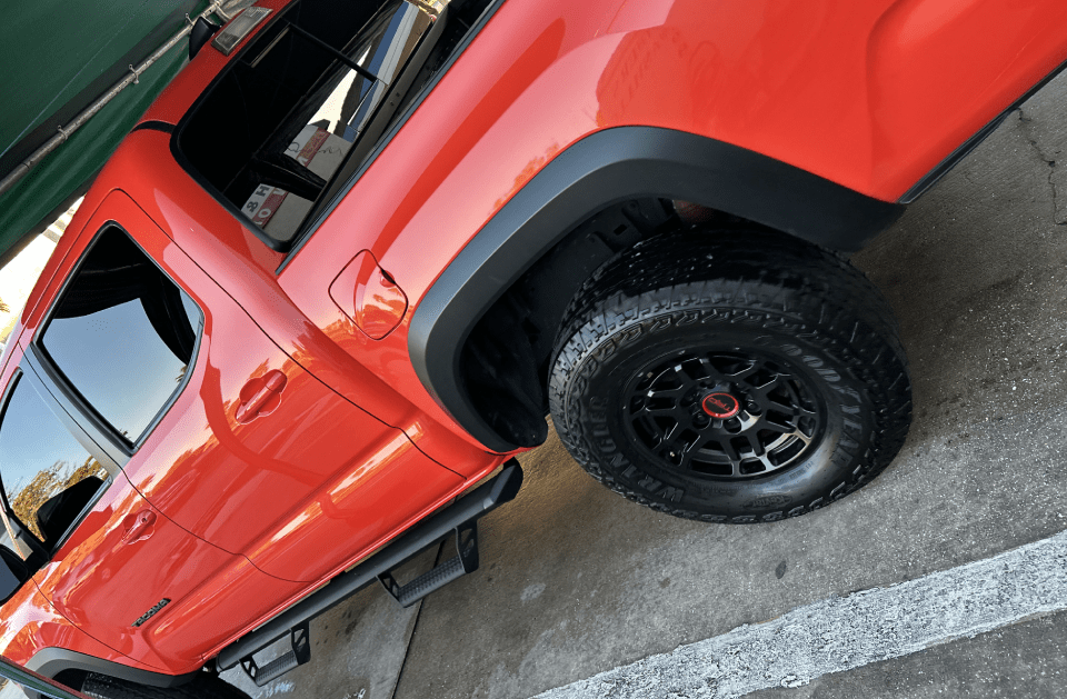 Bright orange Toyota Tacoma truck with black fender flares and wheels.