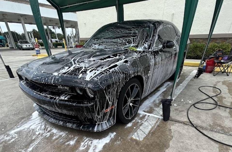 Black Dodge Challenger covered in soap suds at a car wash.