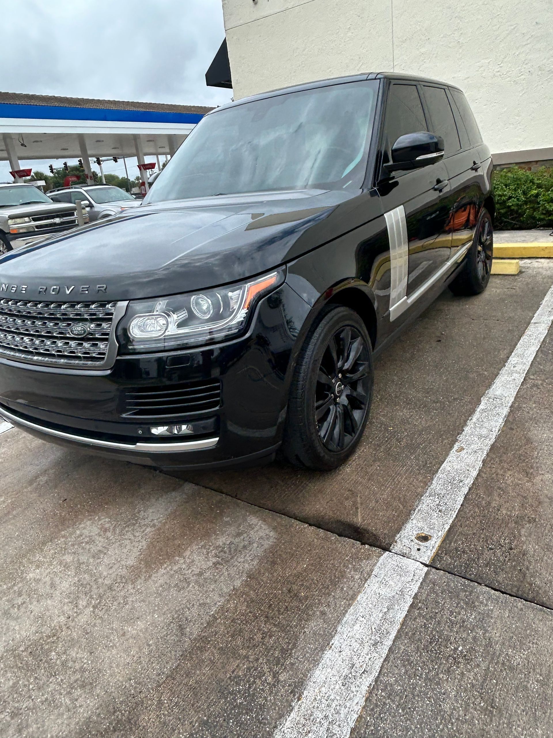 Black Range Rover parked in a white-lined parking spot. Gas station in the background.