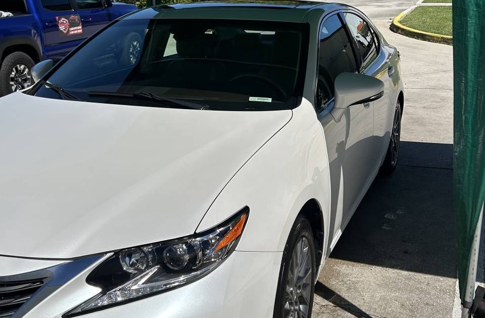 White Lexus sedan parked near a building, under the sunlight.
