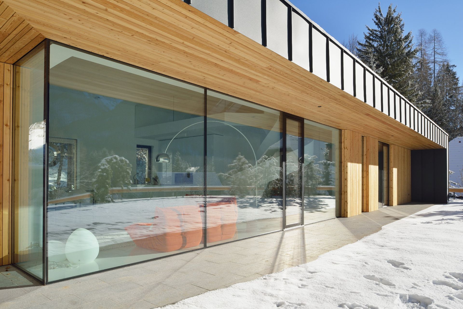 Moderno edificio con facciata in vetro e rivestimento in legno, immerso in un paesaggio innevato dove si riflettono i pini.