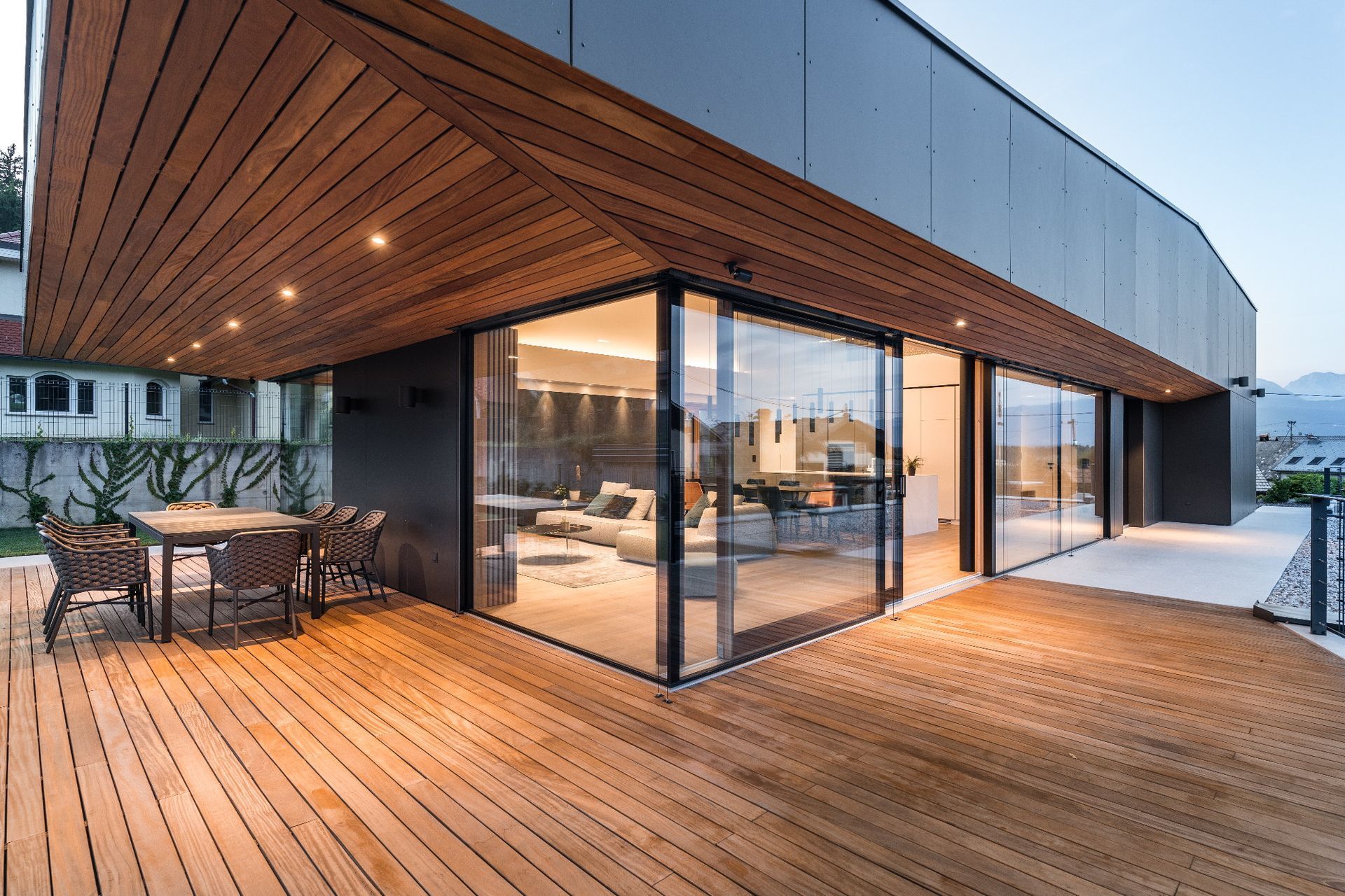 Terrazza moderna con soffitto in legno, pareti in vetro e posti a sedere all'aperto al crepuscolo.
