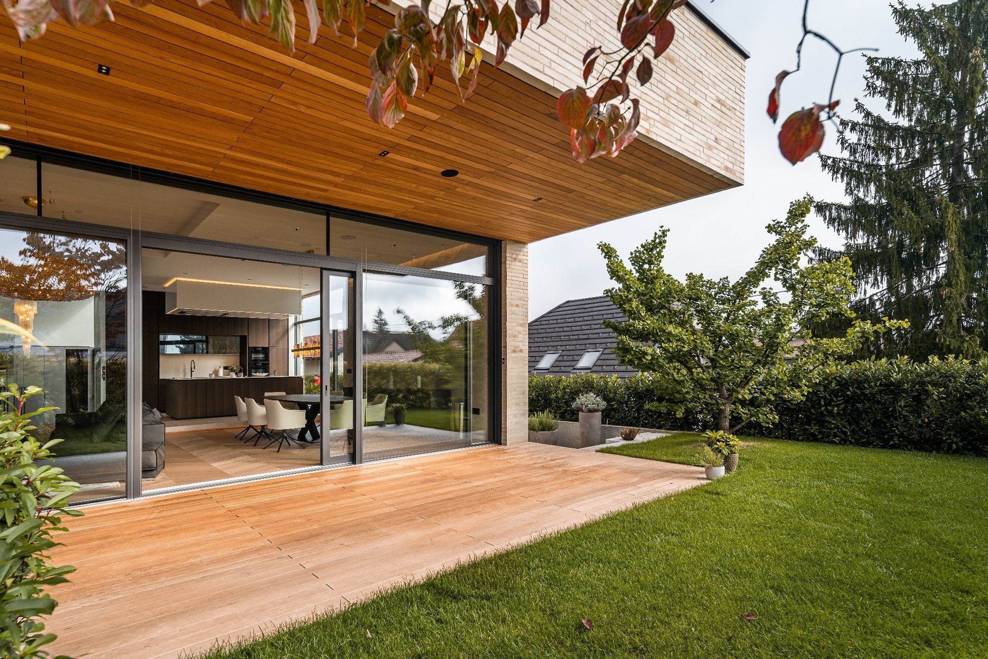 Patio moderno con tettoia in legno, porte scorrevoli in vetro e prato verde accanto alla casa.