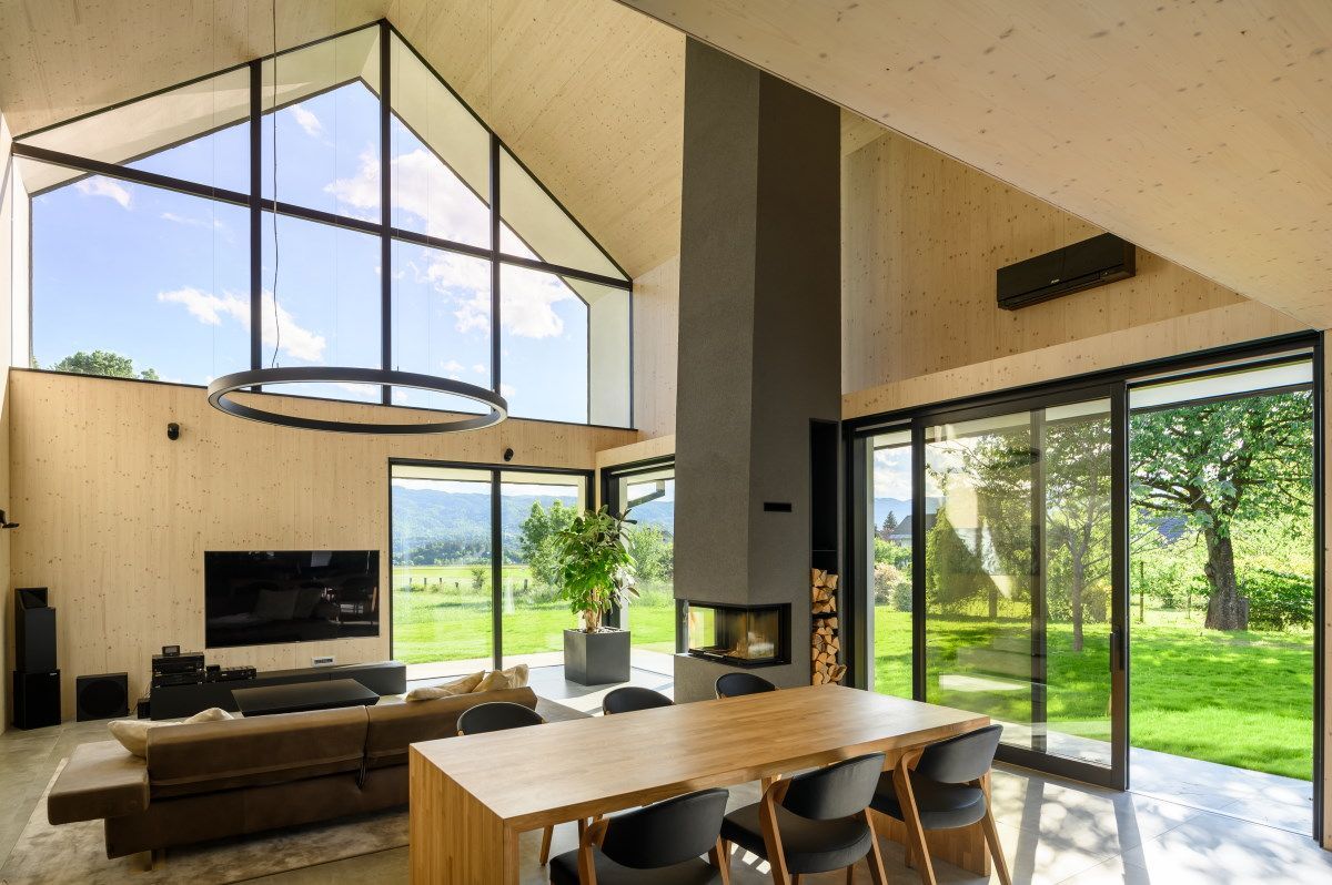 Soggiorno moderno a pianta aperta con ampie finestre, tavolo da pranzo, divano, TV e vista su un giardino verde.