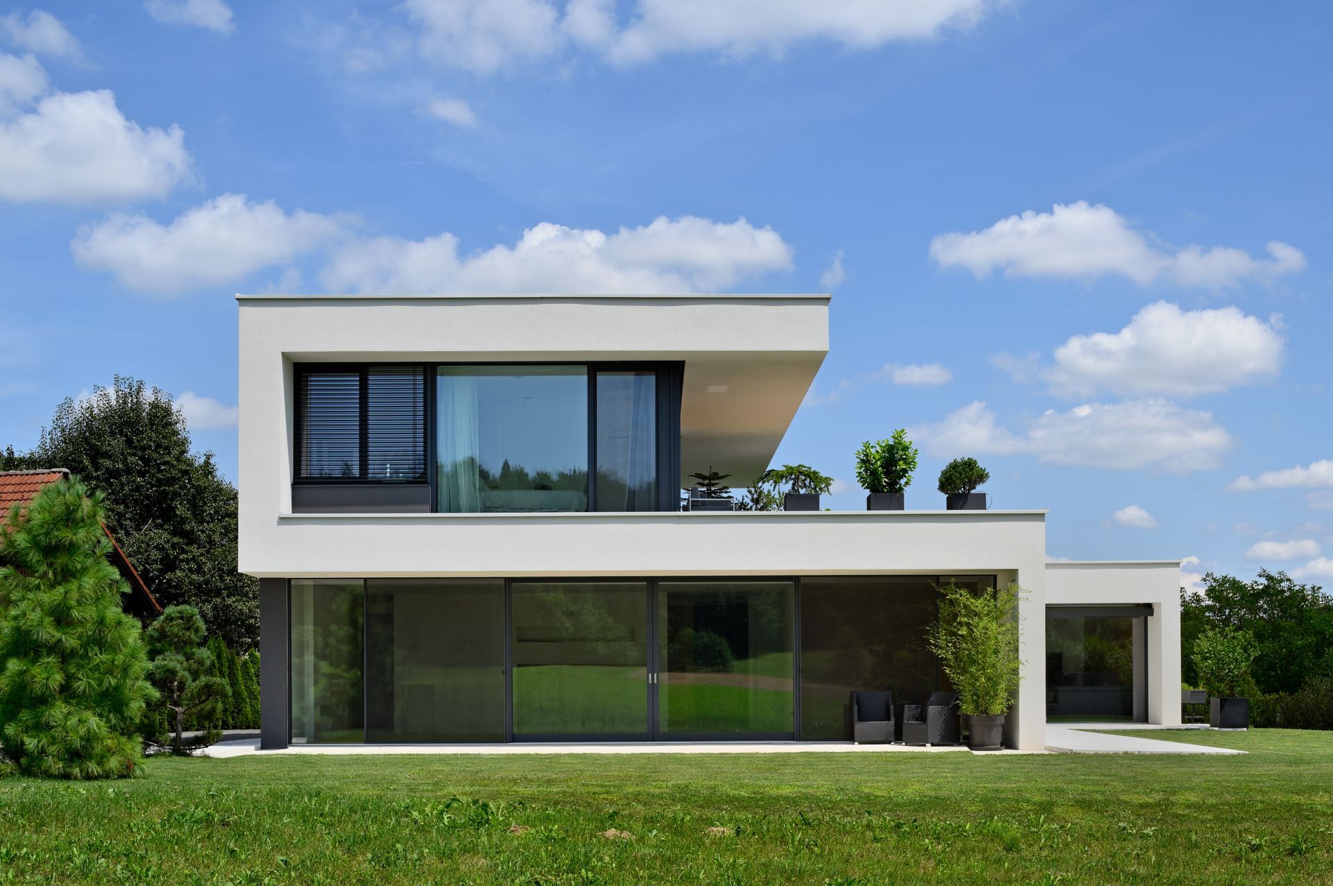 Casa moderna bianca a due piani con grandi finestre e un prato verde sotto un cielo azzurro