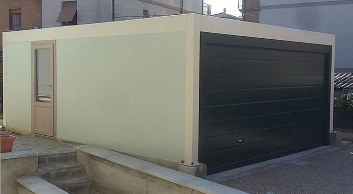 Piccolo garage beige con una porta avvolgibile scura accanto a uno stretto ingresso laterale e una finestra.