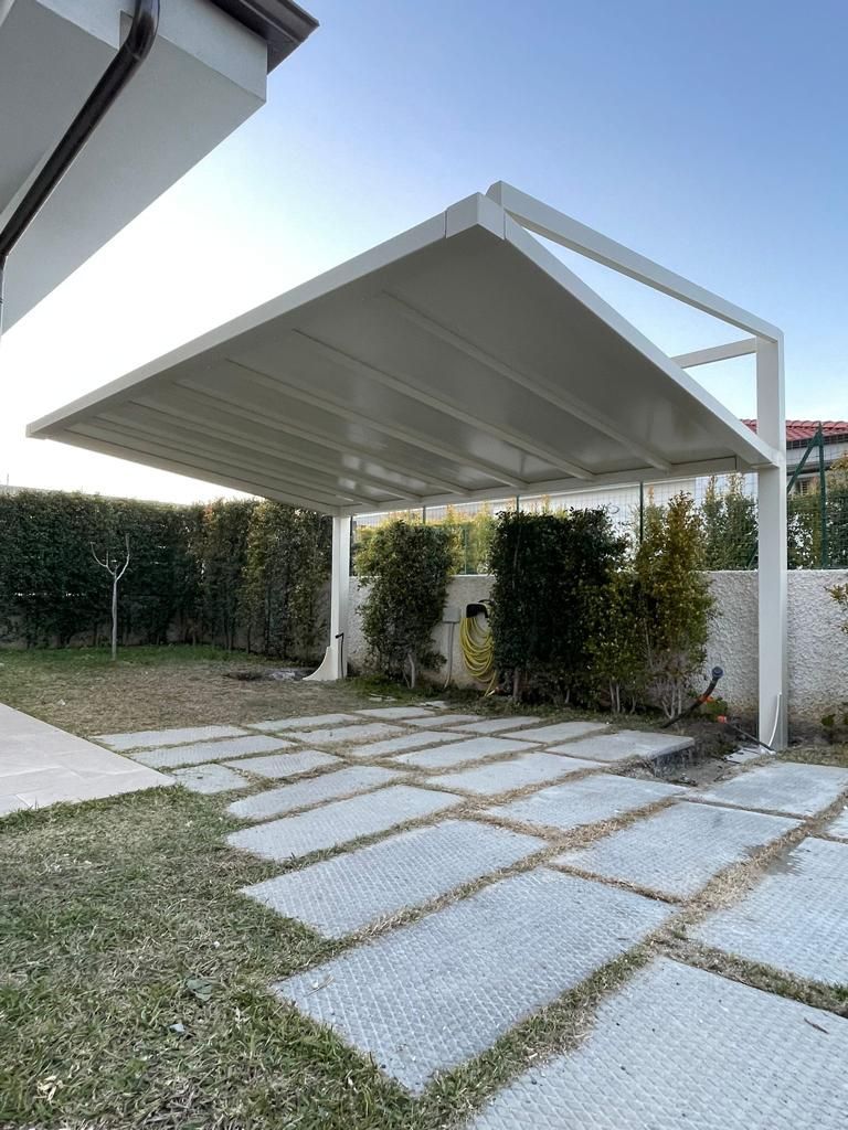 Moderno carport bianco con tetto spiovente sopra pavimentazione in pietra e cortile erboso