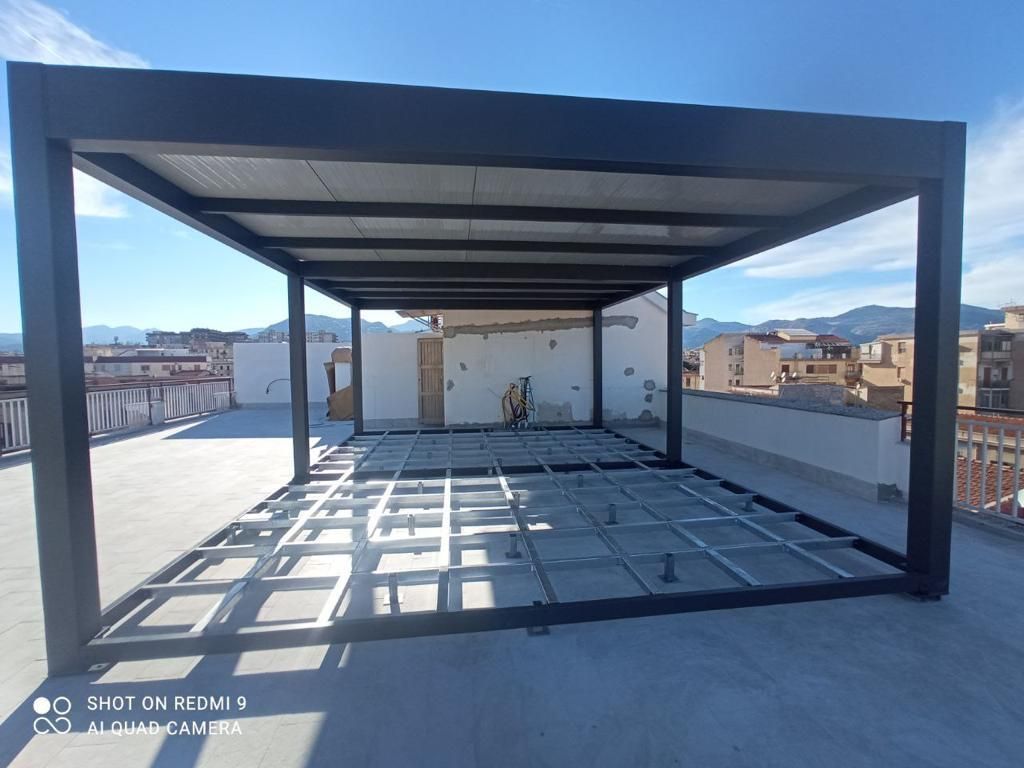 Terrazza sul tetto con pergola in metallo nero che proietta ombre a griglia sul pavimento in cemento.