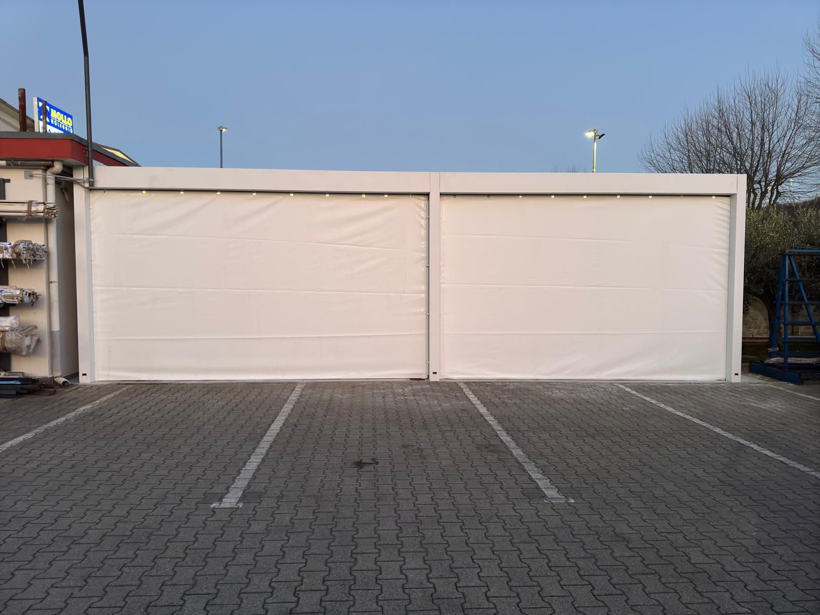 Due portoni industriali bianchi su un piazzale pavimentato sotto un cielo limpido
