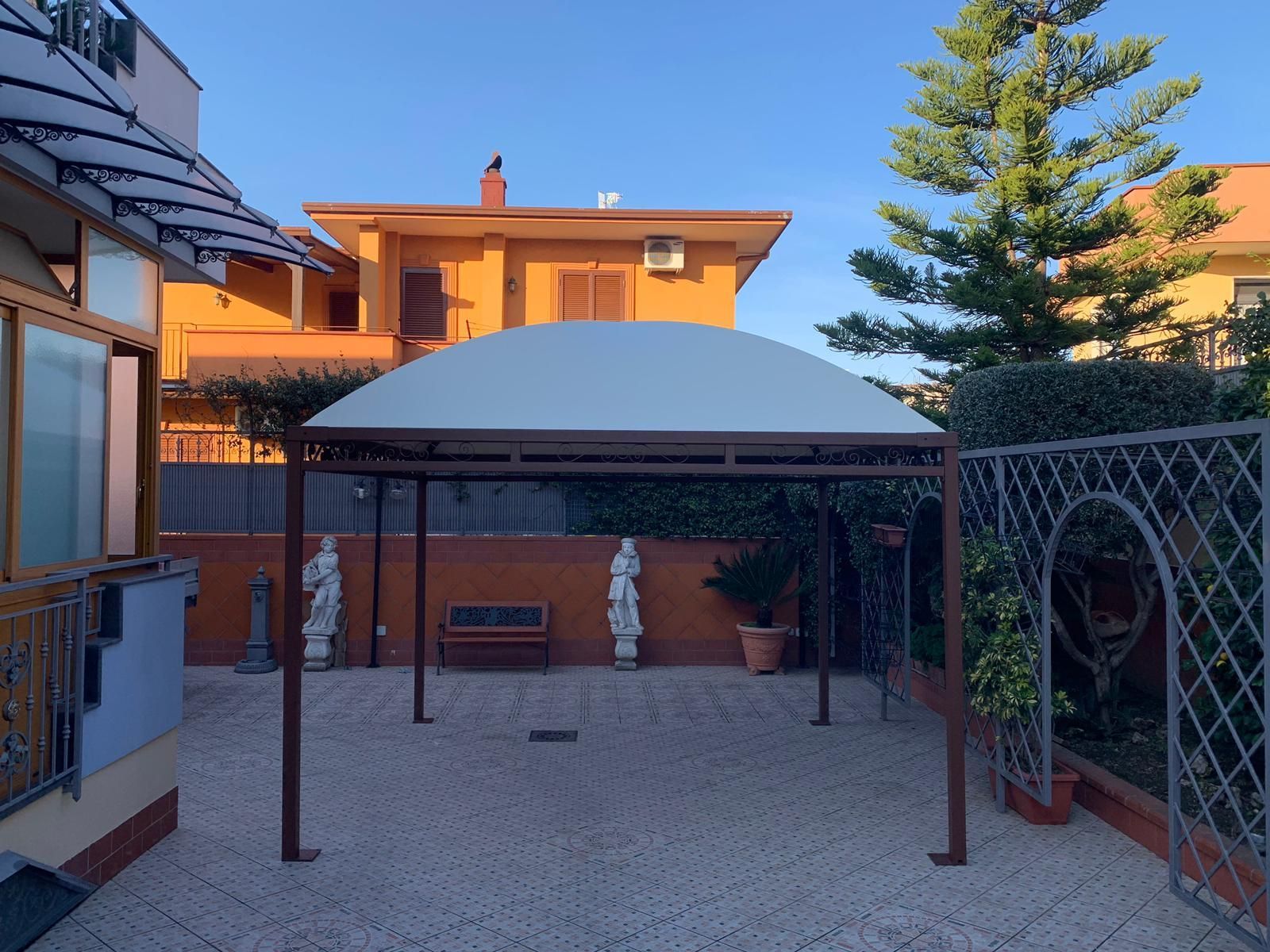 Cortile con patio, tettoia bianca, muri in mattoni e recinzione a traliccio, immerso nella calda luce del sole.