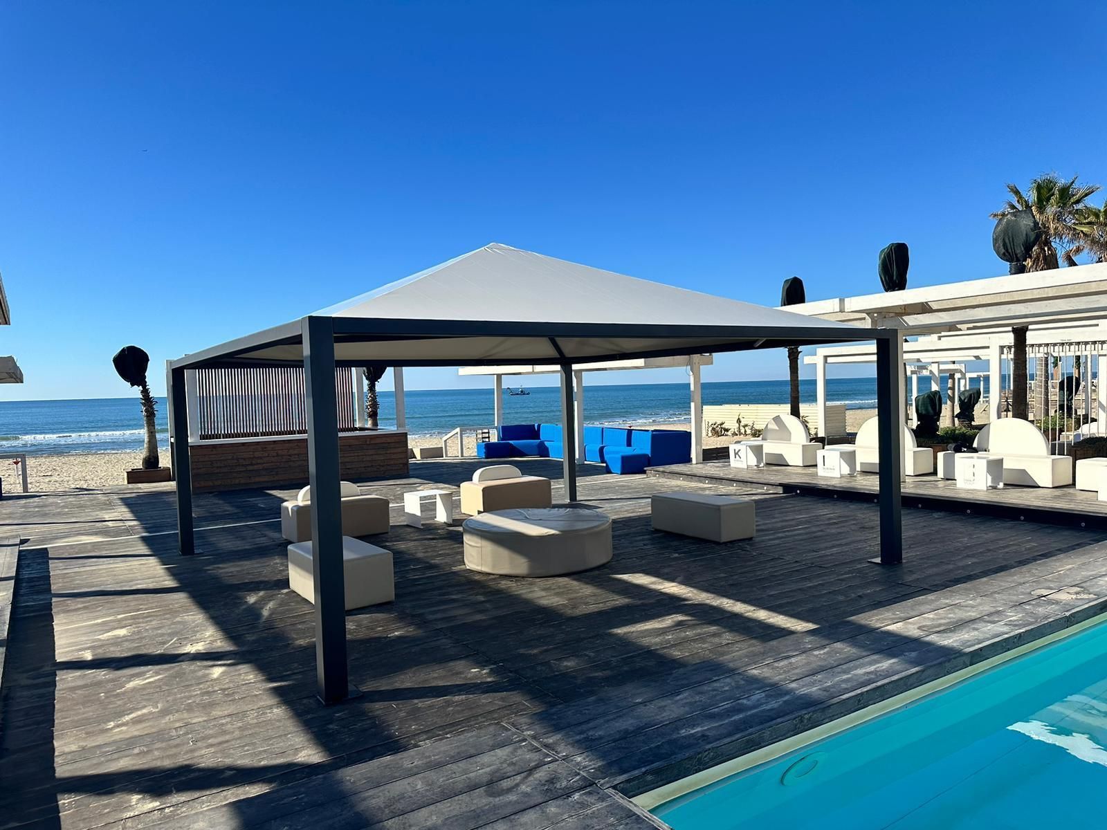 Cabina sulla spiaggia con lettini prendisole a bordo piscina, sotto un cielo limpido.