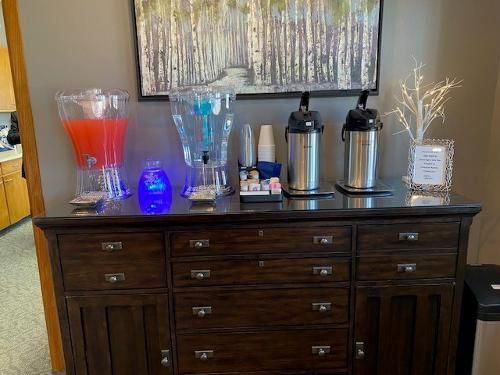 Beverage station on a dark wood cabinet. Drinks include juice, water, coffee. White decorative tree and artwork behind.