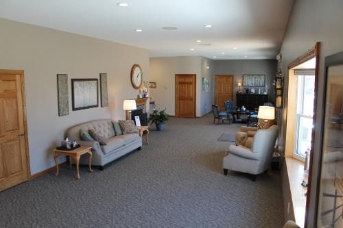 Spacious room with seating areas, fireplace, and two wooden doors. Neutral color scheme, carpeted floors.