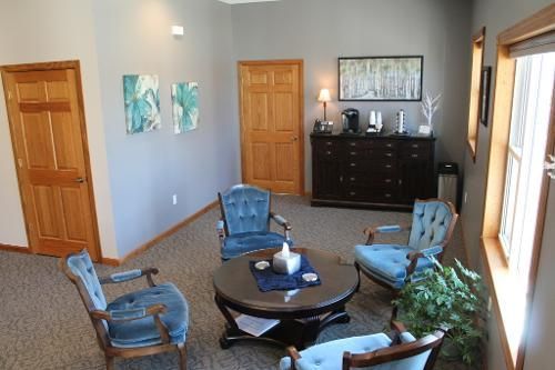 A waiting room with four blue chairs around a table, artwork, and a coffee station.