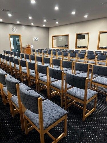 Rows of blue upholstered chairs in a meeting room, neutral walls, carpet.