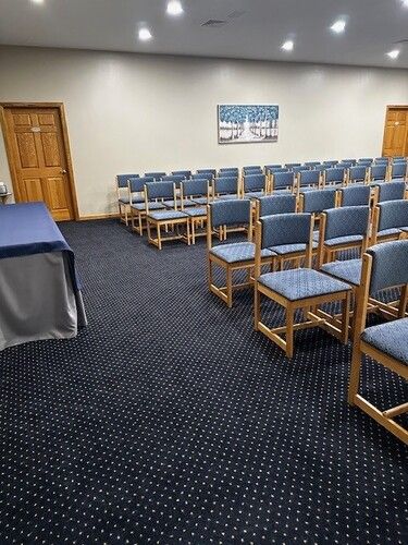 Rows of blue chairs in a conference room with navy blue carpet, beige walls, and a small painting.