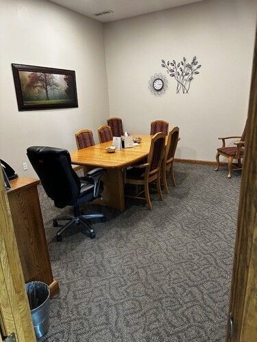 Conference room with wooden table, chairs, and painting. Neutral color walls, carpeted floor.