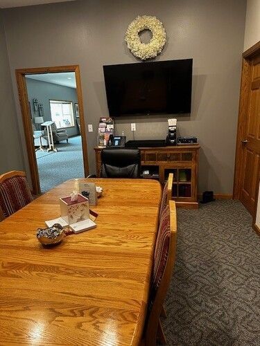A room with a long wooden table, a TV on the wall, and a doorway leading to another area.
