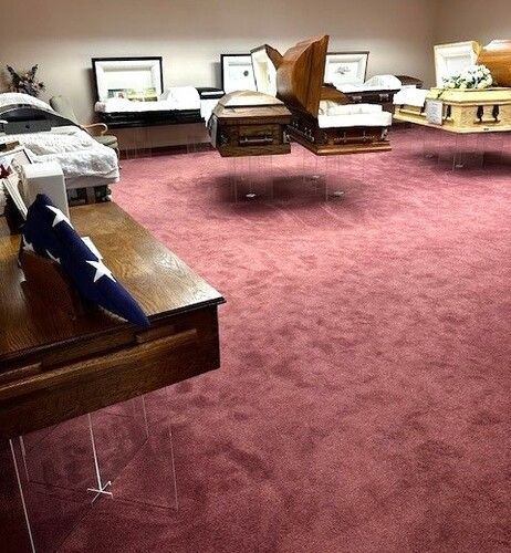 Caskets floating in a room with pink carpet. A folded American flag rests on a wooden surface.