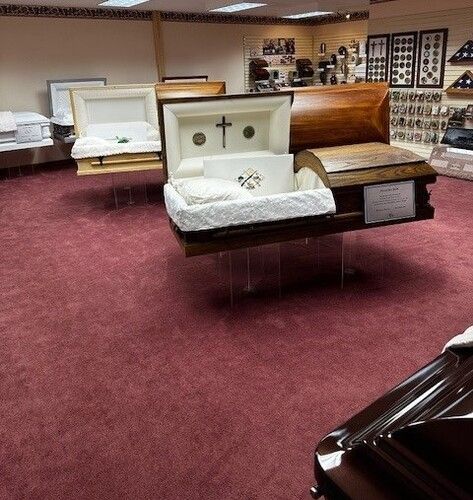 Coffins on display in a funeral home showroom, on red carpet.