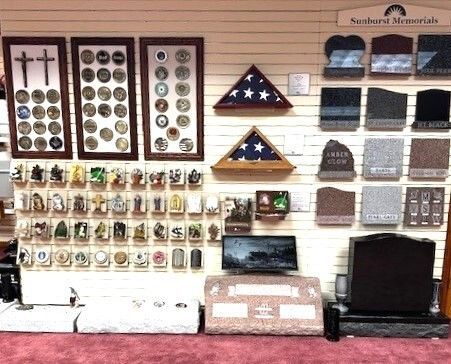 Memorial products display: framed coins, flags, figurines, headstones, and monuments in a showroom setting.