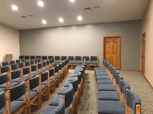 Rows of blue cushioned chairs in an empty room with a door and grey wall.