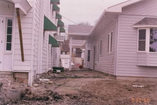 Buildings under construction with dirt ground between them. White siding, green awnings.